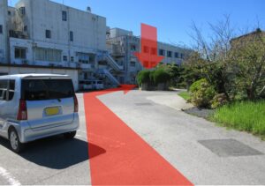 施設周辺の駐車場と建物外観。赤いラインが引かれたアスファルト舗装エリア